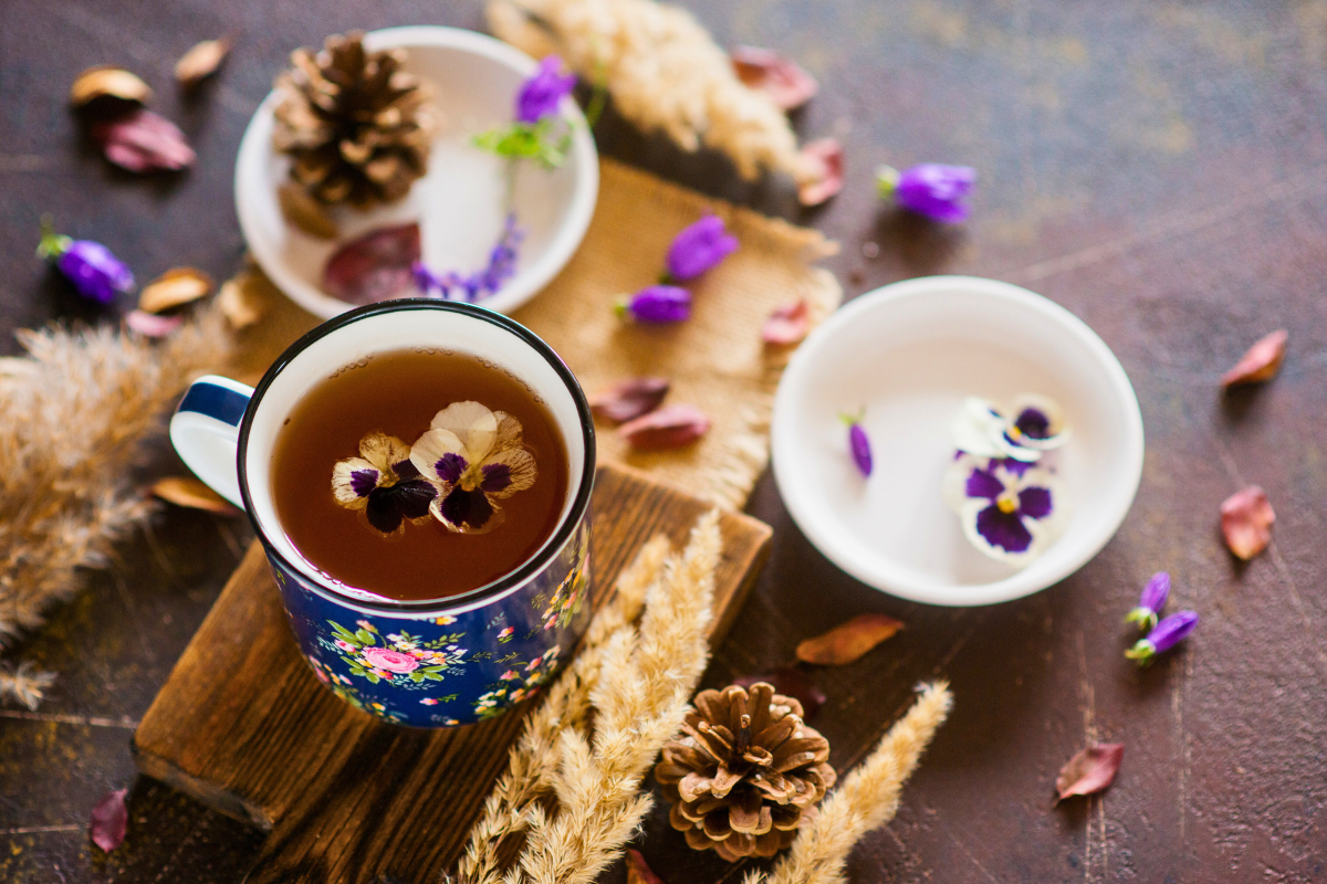 Tea cup with floral decorations on a wooden surface with dried plants and flowers.