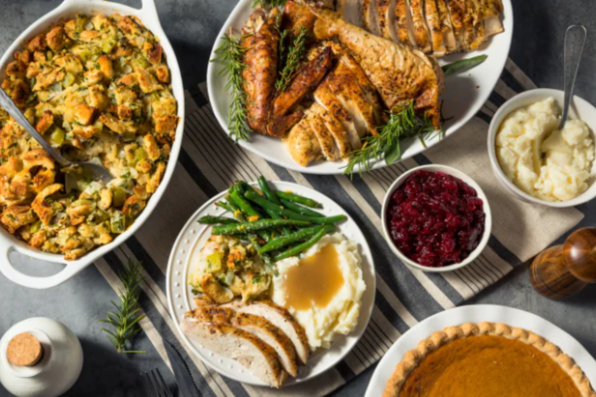 Dinner table set with plates of roasted turkey, stuffing, green beans, cranberry sauce, mashed potatoes