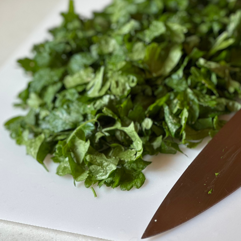 Chopped green parsley piled on a white cutting board next to a  knife blade.